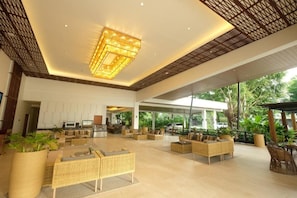 A spacious lobby with wicker furniture, a large chandelier, and a view of greenery outside.