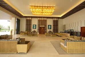A spacious lobby with a large chandelier, wicker furniture, and a reception desk. - The Tropics at Macarthur Park (Palo)