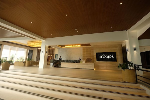 A hotel lobby with a reception desk, a wooden ceiling, and a sign that reads 'Tropics'.