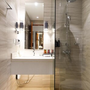 A modern bathroom with a glass-enclosed shower, a white vanity with a mirror, and a handheld showerhead. - The Tropics at Macarthur Park (Palo)