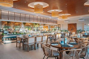 Un restaurante con mesas redondas, sillas de mimbre y lámparas colgantes.
