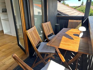 A wooden deck with a table and chairs, a small white stool, and a glass door leading to an outdoor area. - Alpenblick.Hoch3 Vacation rental with two separate bedrooms and three balconies facing east-southwest (Aschau im Chiemgau)