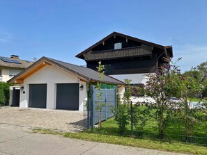 A two-story house with a garage, a small attached structure, and a fenced garden area. - Alpenblick.Hoch3 Vacation rental with two separate bedrooms and three balconies facing east-southwest (Aschau im Chiemgau)
