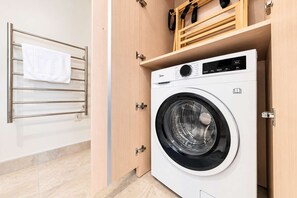 Ein moderner Waschraum mit einer Waschmaschine mit Frontlader, einem Handtuchhalter und Holzschränken.