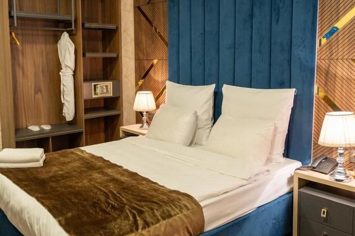 A hotel room with a bed, bedside tables, a wardrobe, and a blue headboard.