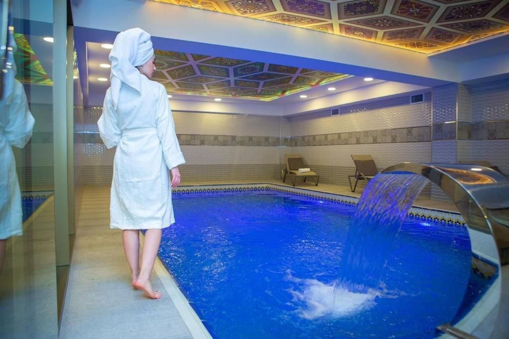 En person i en hvid badekåbe står ved en pool med et vandfald.