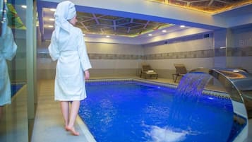 En person i en hvid badekåbe står ved en pool med et vandfald.