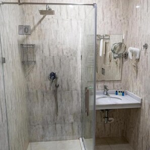 Un baño moderno con ducha de vidrio, lavamanos con espejo y artículos de aseo.