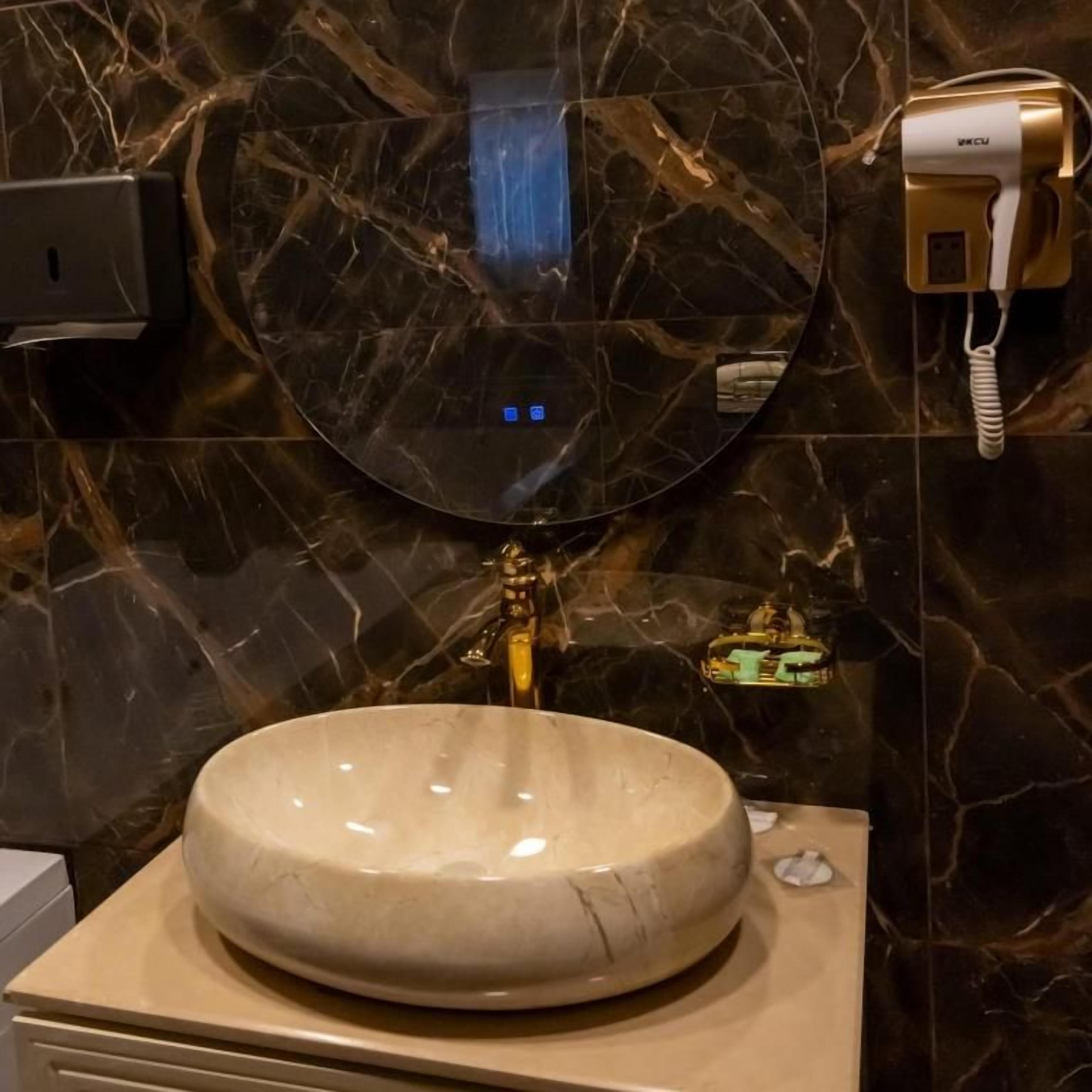 A bathroom with a round mirror, a sink, and a hairdryer on the wall.