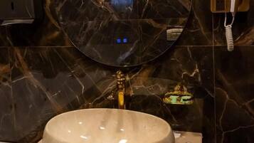 A bathroom with a round mirror, a sink, and a hairdryer on the wall.