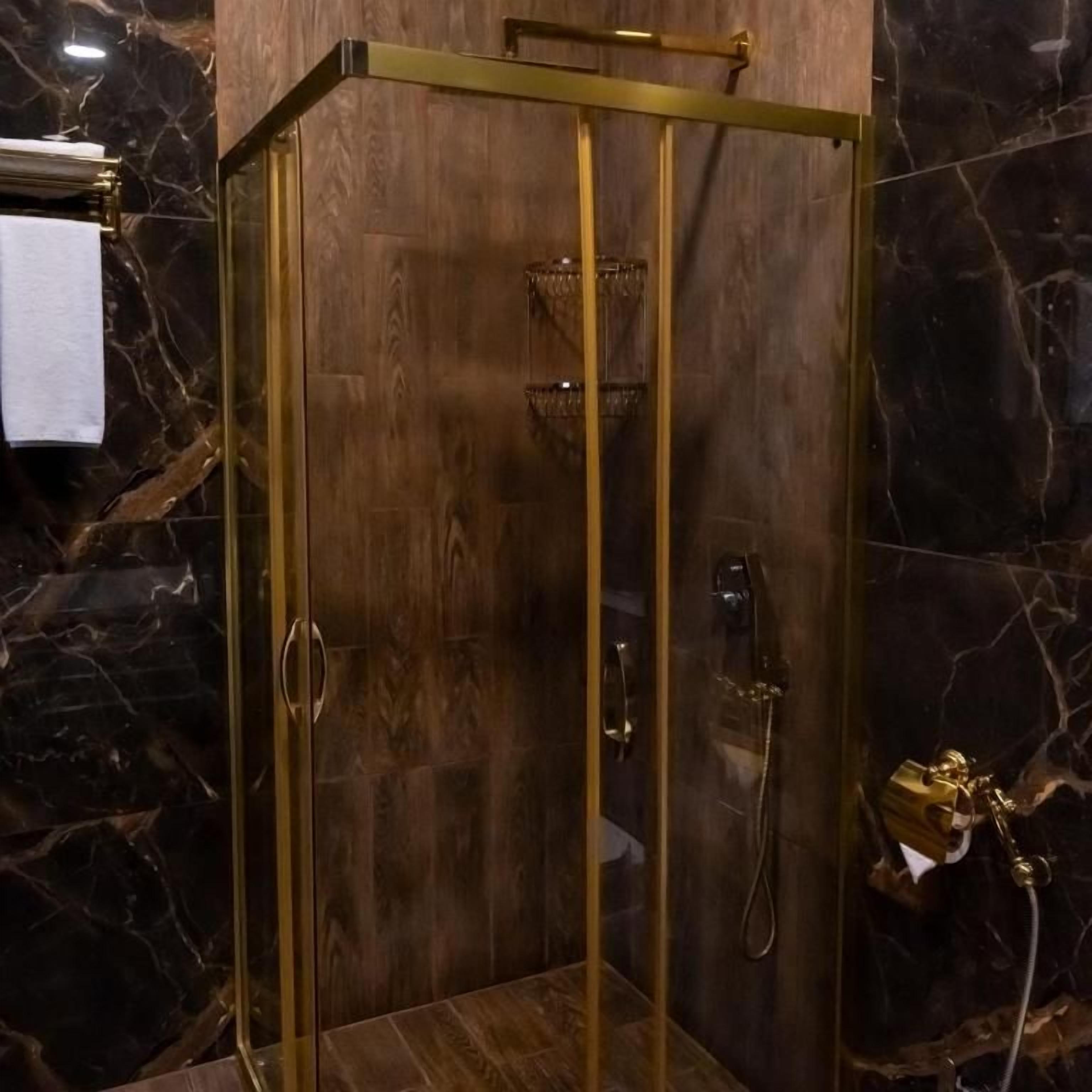 A shower enclosure with a glass door and a gold frame, set against a marble wall.