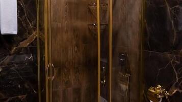 A shower enclosure with a glass door and a gold frame, set against a marble wall.