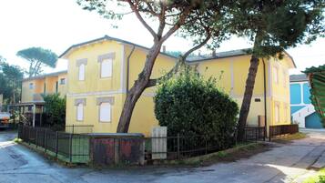 Um edifício amarelo com portão fechado, uma área cercada pequena e uma árvore na frente.