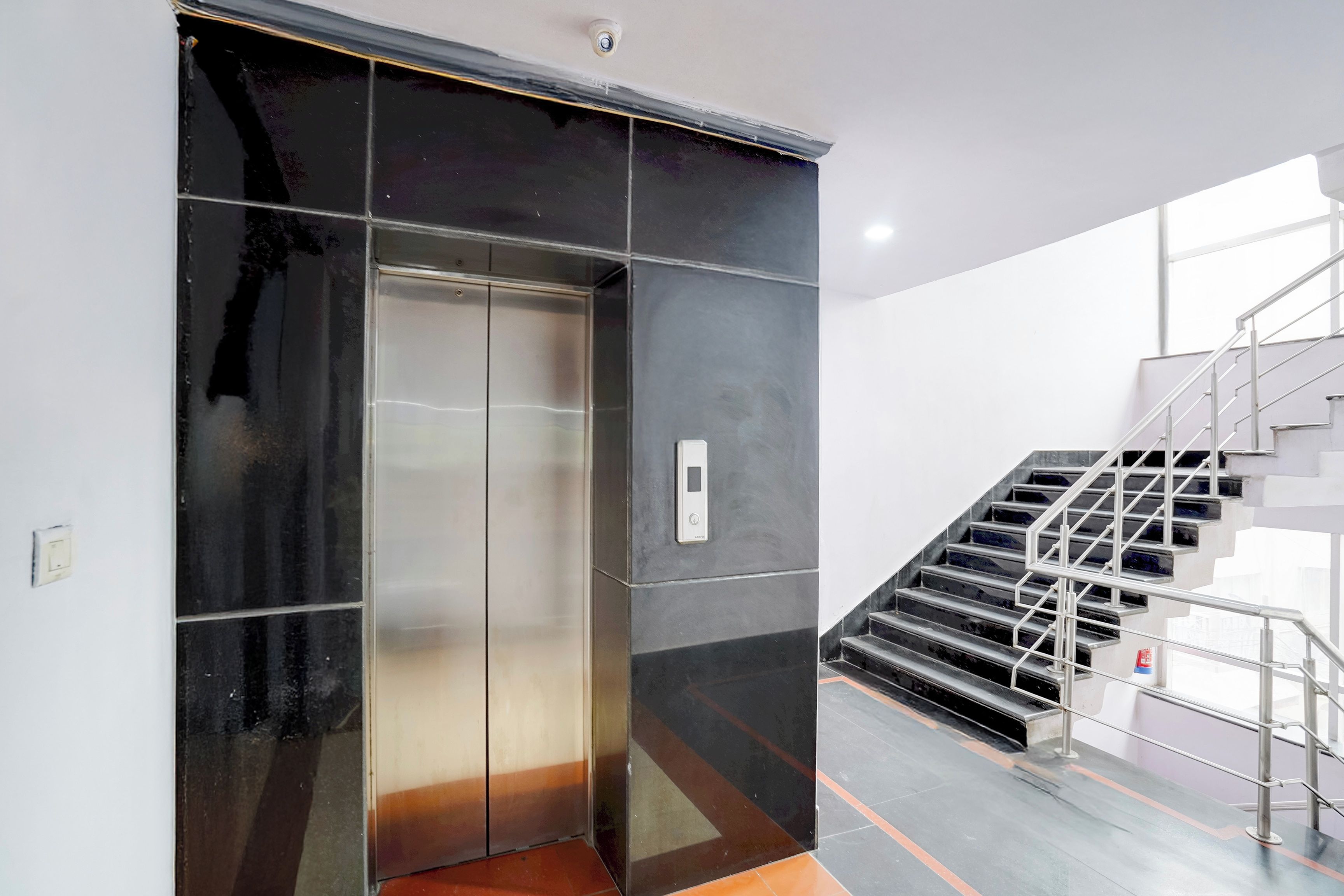 Ein moderner Aufzug mit Metallverkleidung neben einer Treppe mit Metallgeländern.