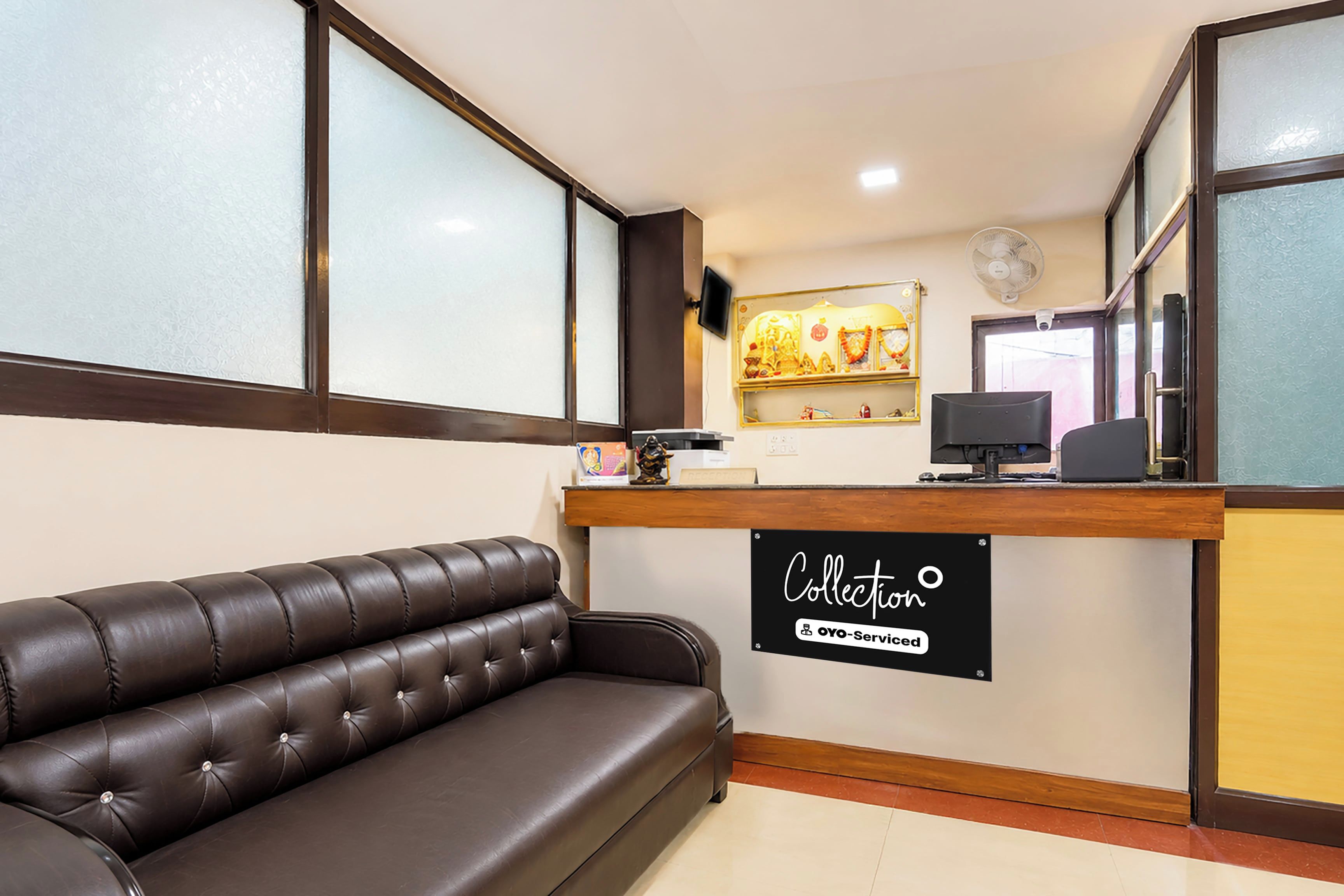 A reception area with a leather sofa, a reception desk, a computer, and a wall-mounted fan.