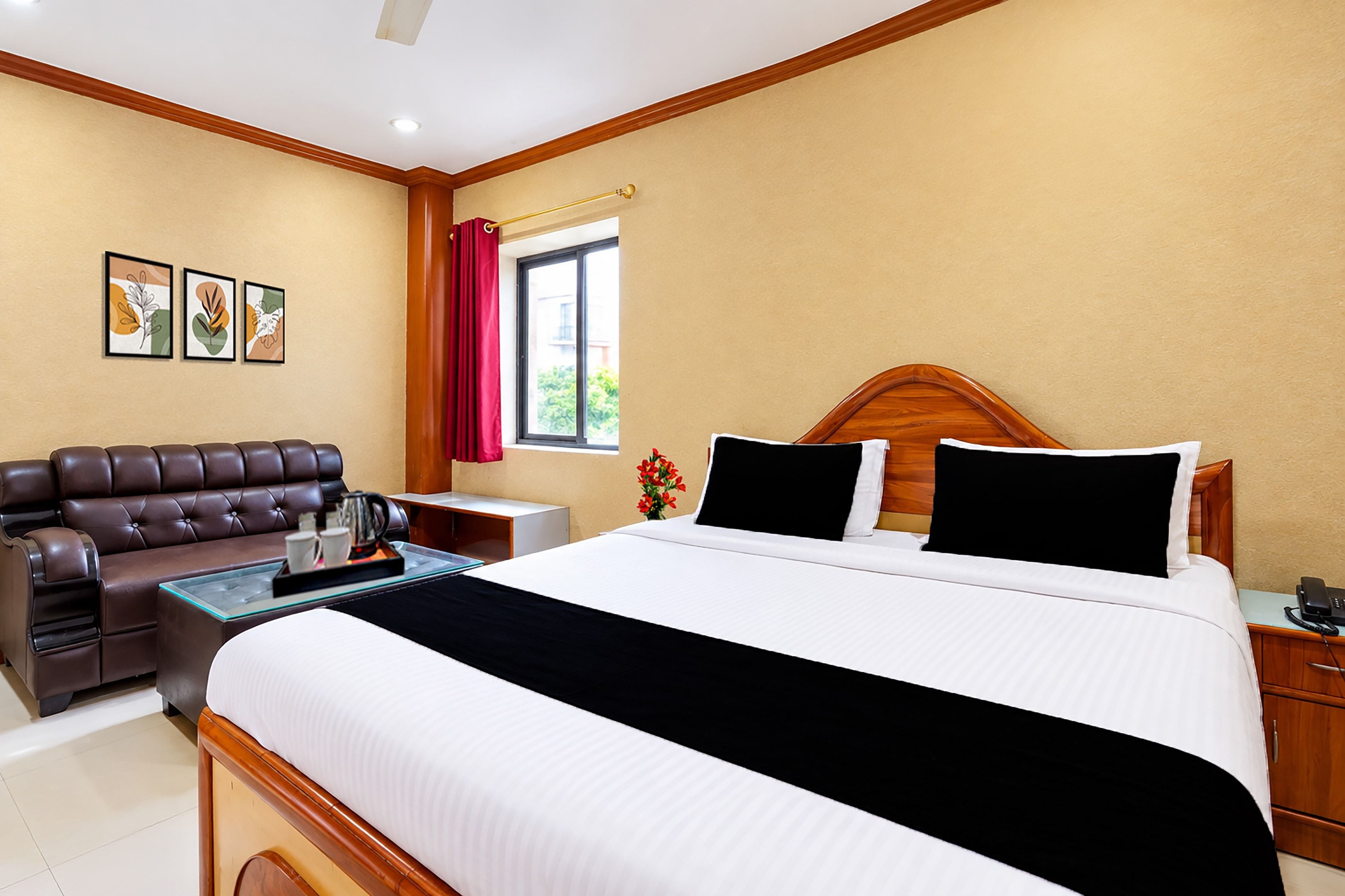 Quarto de hotel com cama, sofá de couro, mesinha com bandeja, mesa de cabeceira e janela com vista.