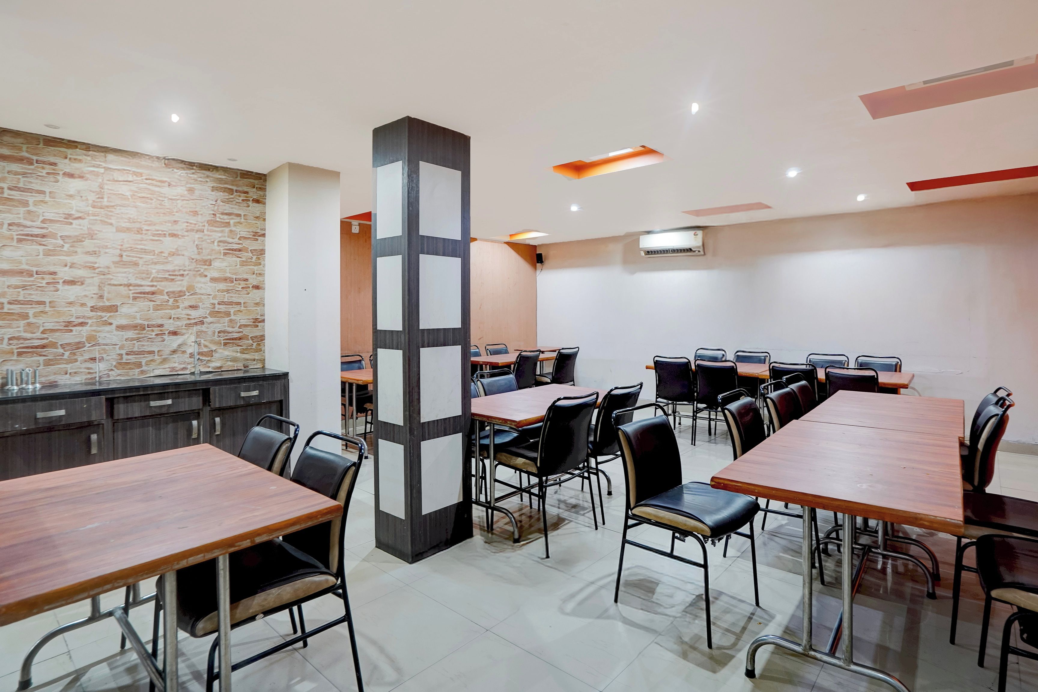 A conference room with multiple tables and chairs, a stone wall, and a modern ceiling design.