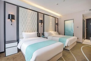 Ein Hotelzimmer mit zwei Betten, einem großen gepolsterten Kopfteil, Wandleuchten und einer Tür mit Milchglasfenster.