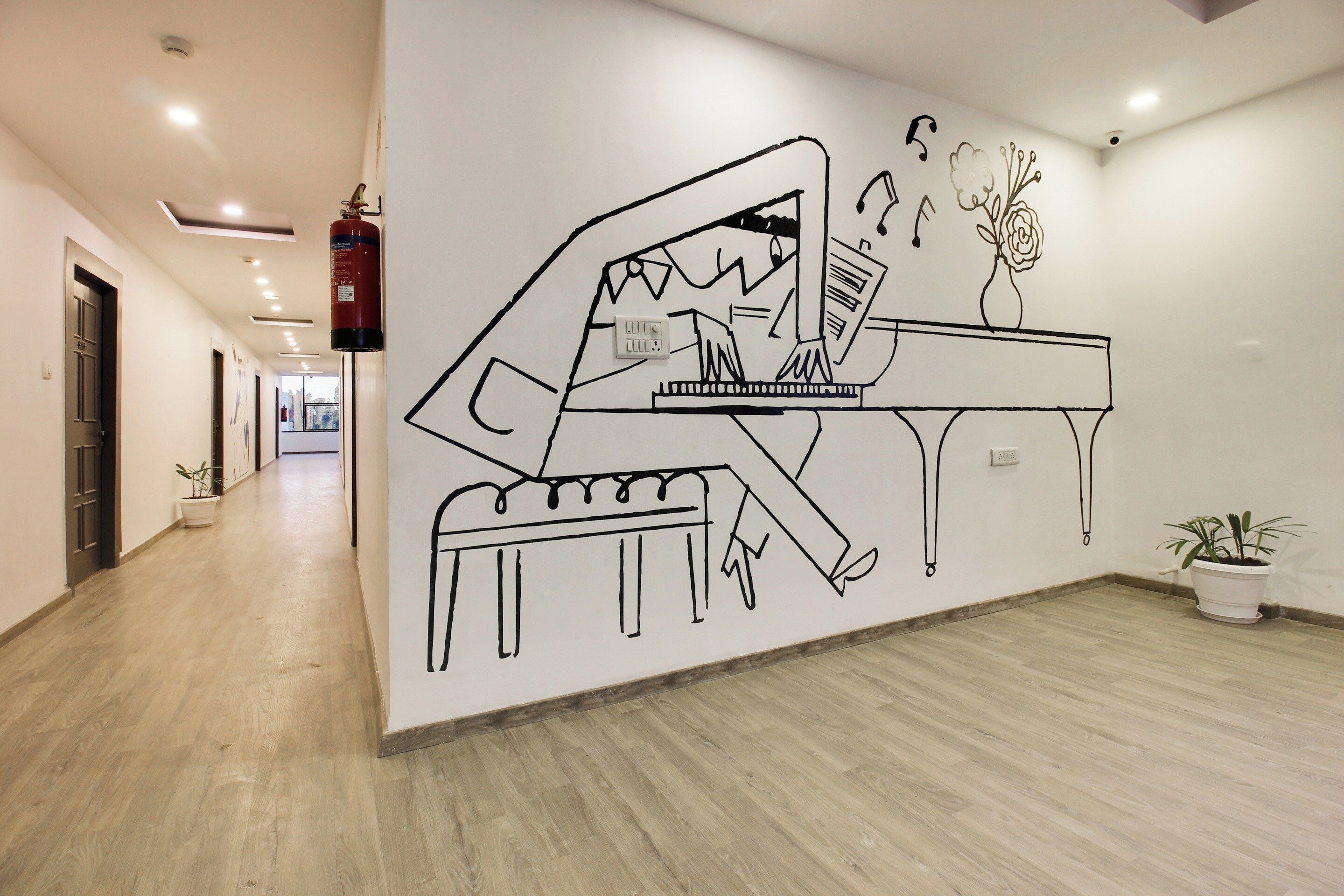 A hallway with a wall mural of a piano, a fire extinguisher, and potted plants.