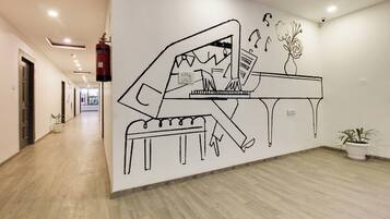 Un pasillo con un mural de un piano, un extintor y plantas en macetas.