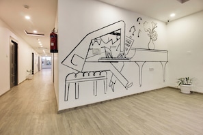 En hall med en väggmålning som föreställer ett piano, en brandsläckare och krukväxter.