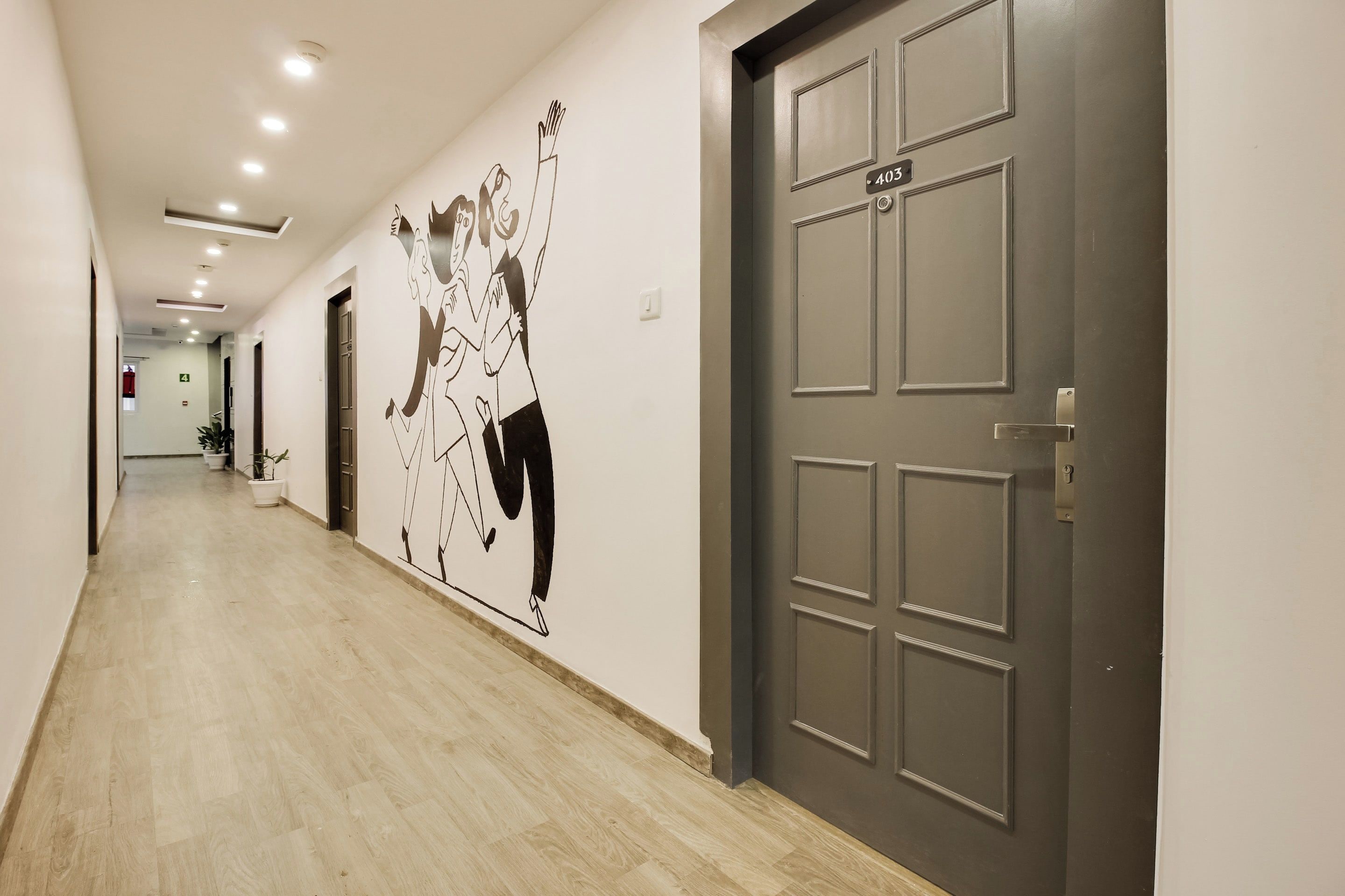 A hallway with a light-colored floor, a door with a number plate, and a wall with a black and white mural.