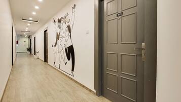 A hallway with a light-colored floor, a door with a number plate, and a wall with a black and white mural.