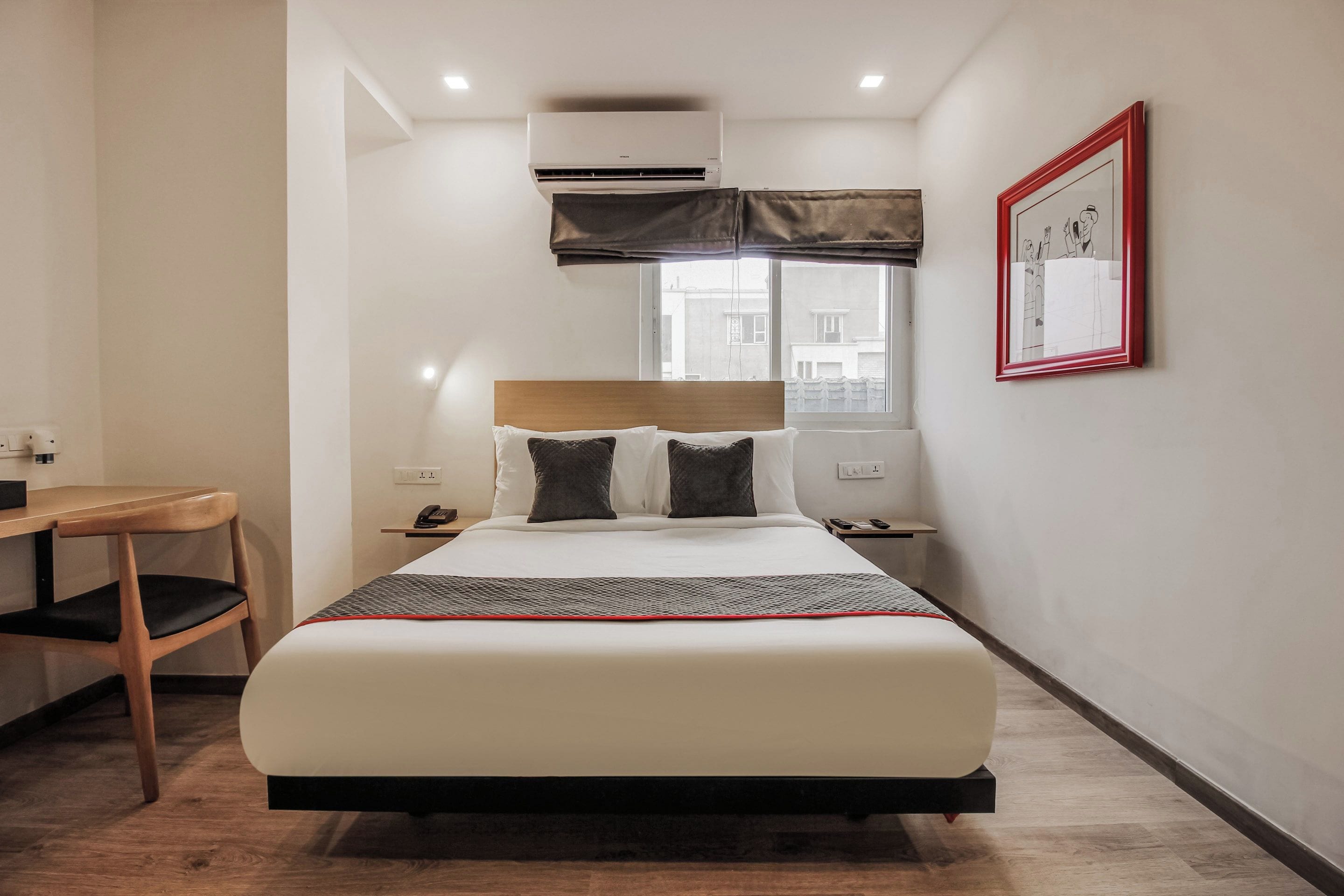 Quarto de hotel com cama, mesa de cabeceira, escrivaninha e ar condicionado.