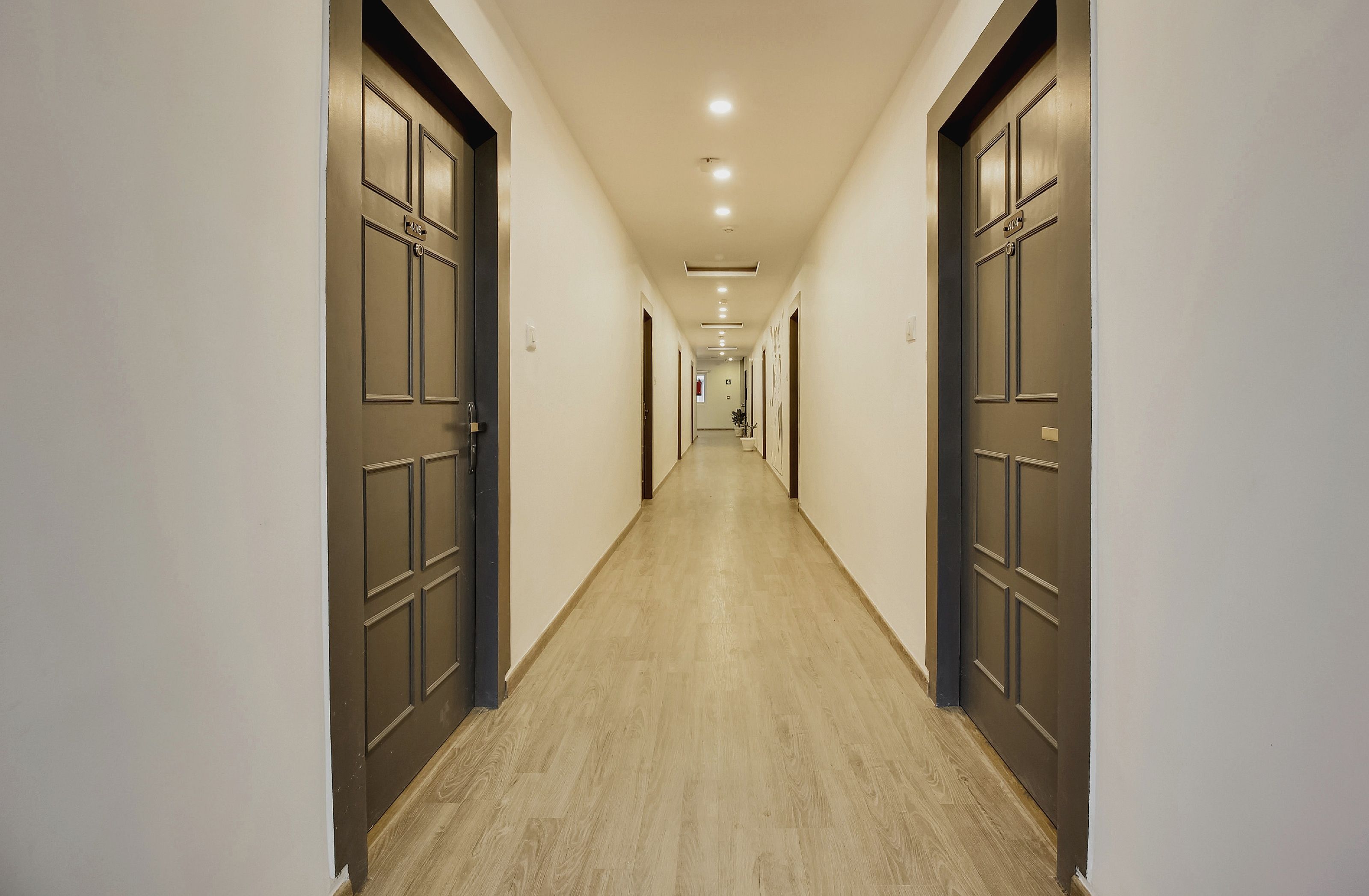 Pasillo de hotel con puertas a ambos lados, piso de madera clara e iluminación empotrada en el techo.