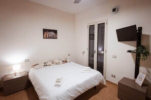 A hotel room with a bed, a flat-screen TV mounted on the wall, a nightstand, a bedside table, and a framed picture on the wall.