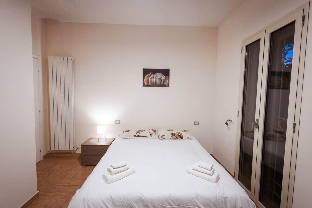 Ein Hotelzimmer mit einem Bett, einem Nachttisch, einem Heizkörper, einem Bild an der Wand und einer Schiebetür.