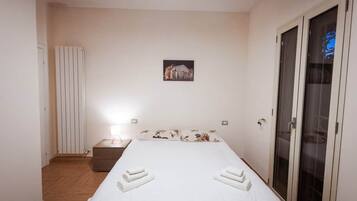 Ein Hotelzimmer mit einem Bett, einem Nachttisch, einem Heizkörper, einem Bild an der Wand und einer Schiebetür.