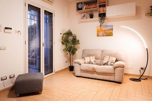 A living room with a sofa, a potted plant, a bookshelf, and a door.