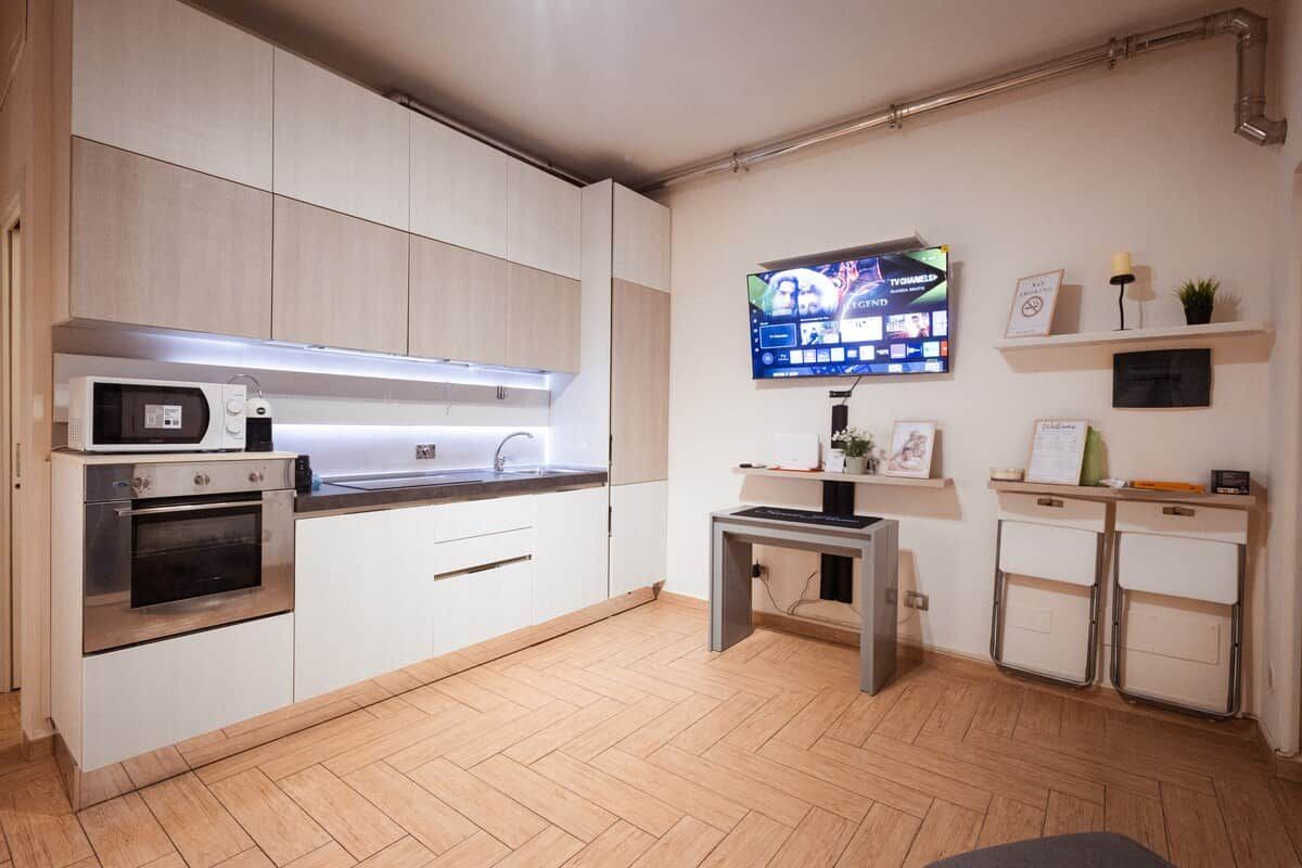 A modern kitchen with a built-in oven, microwave, and a flat-screen TV mounted on the wall.