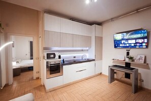 Eine moderne Küche mit weißen Schränken, einem Einbauofen und einem flachbildfernseher an der Wand.