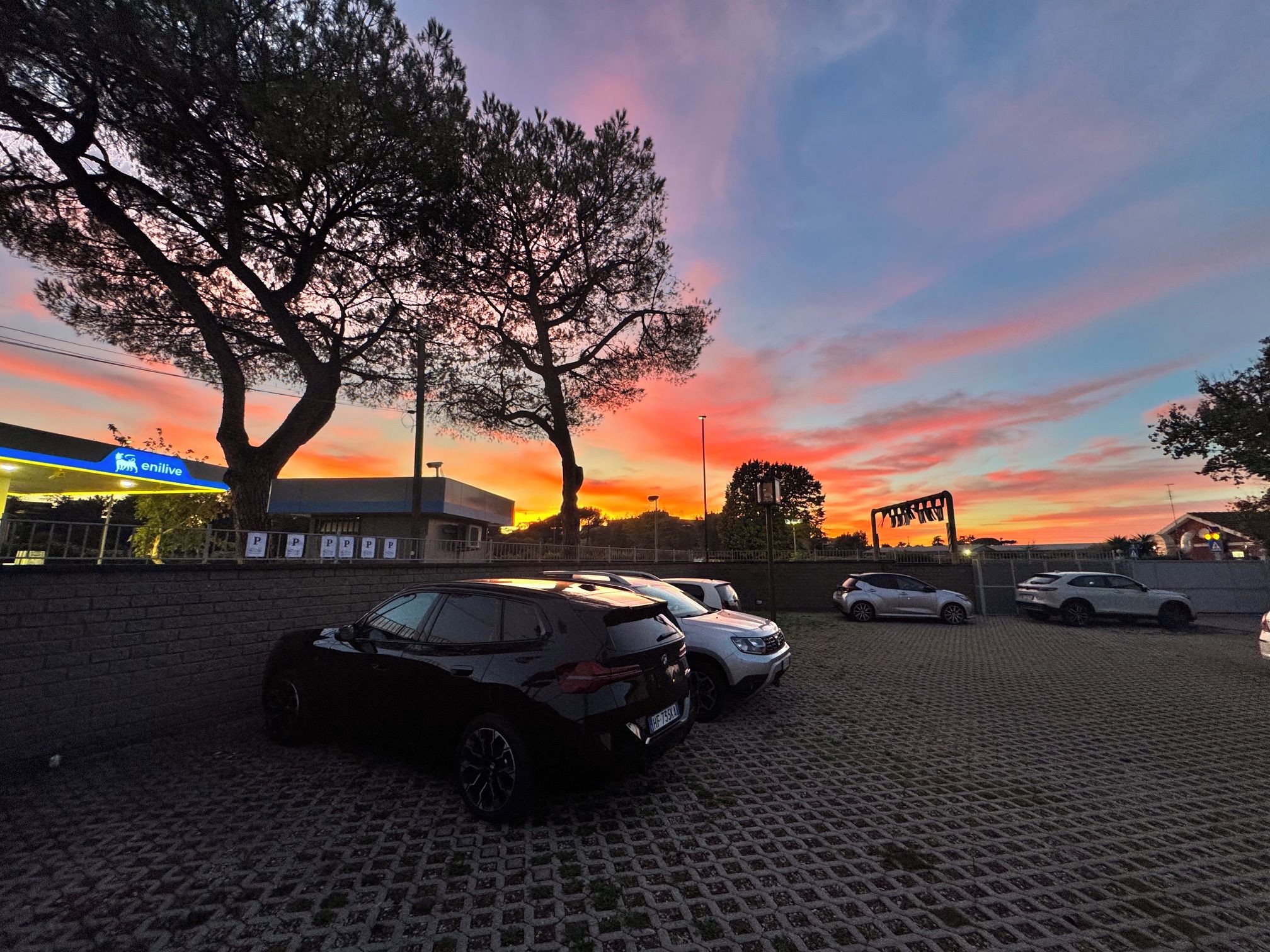 A parking lot with cars, a gas station, and a sunset in the background.