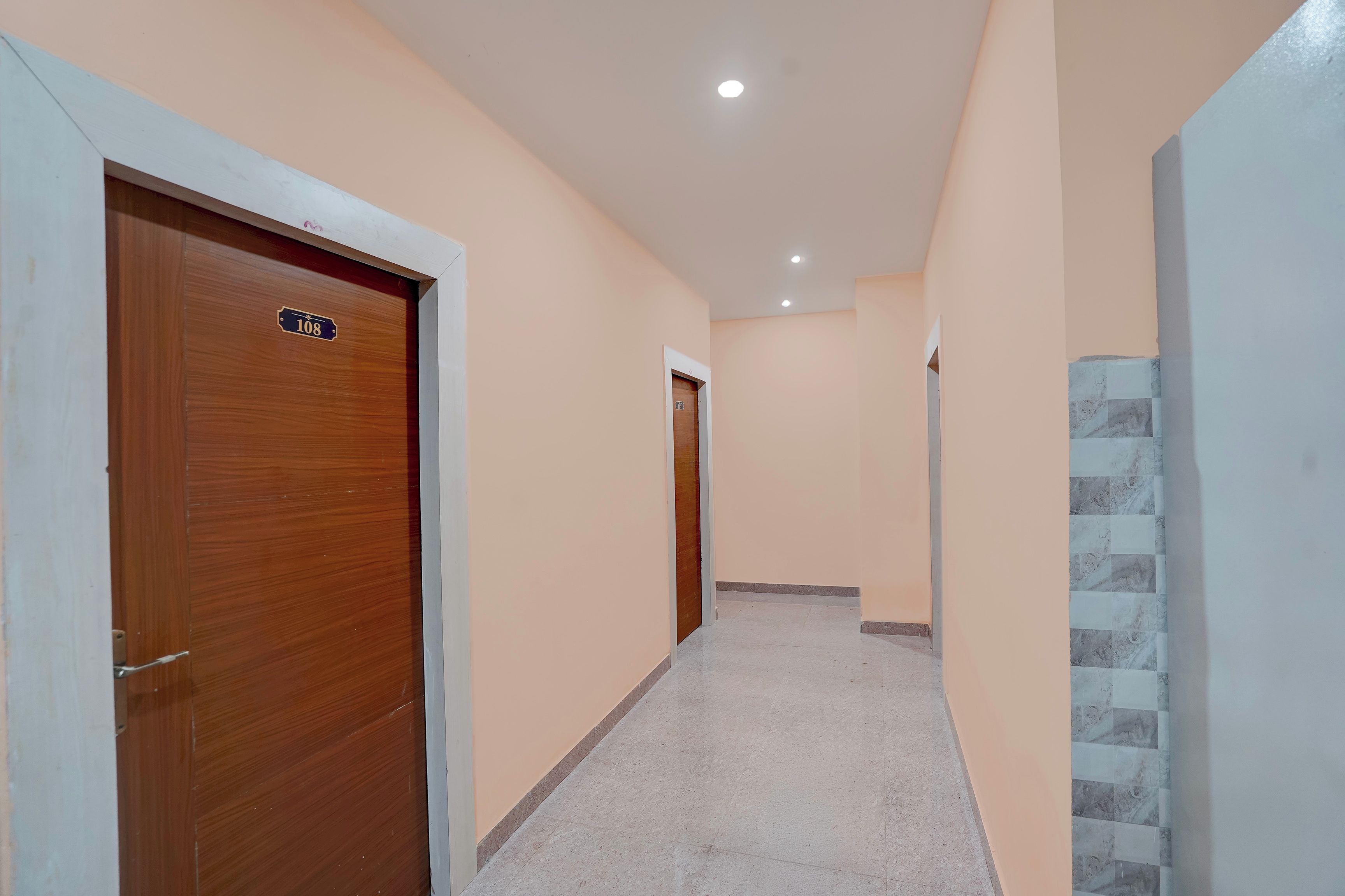 Un pasillo con puertas de madera, suelo de baldosas y pared de color claro.