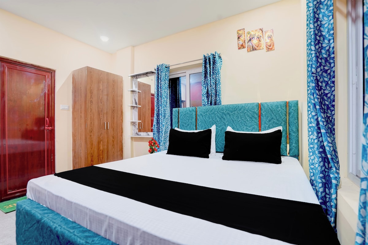 A bedroom with a bed, a wardrobe, a window with curtains, and a wall with artwork.