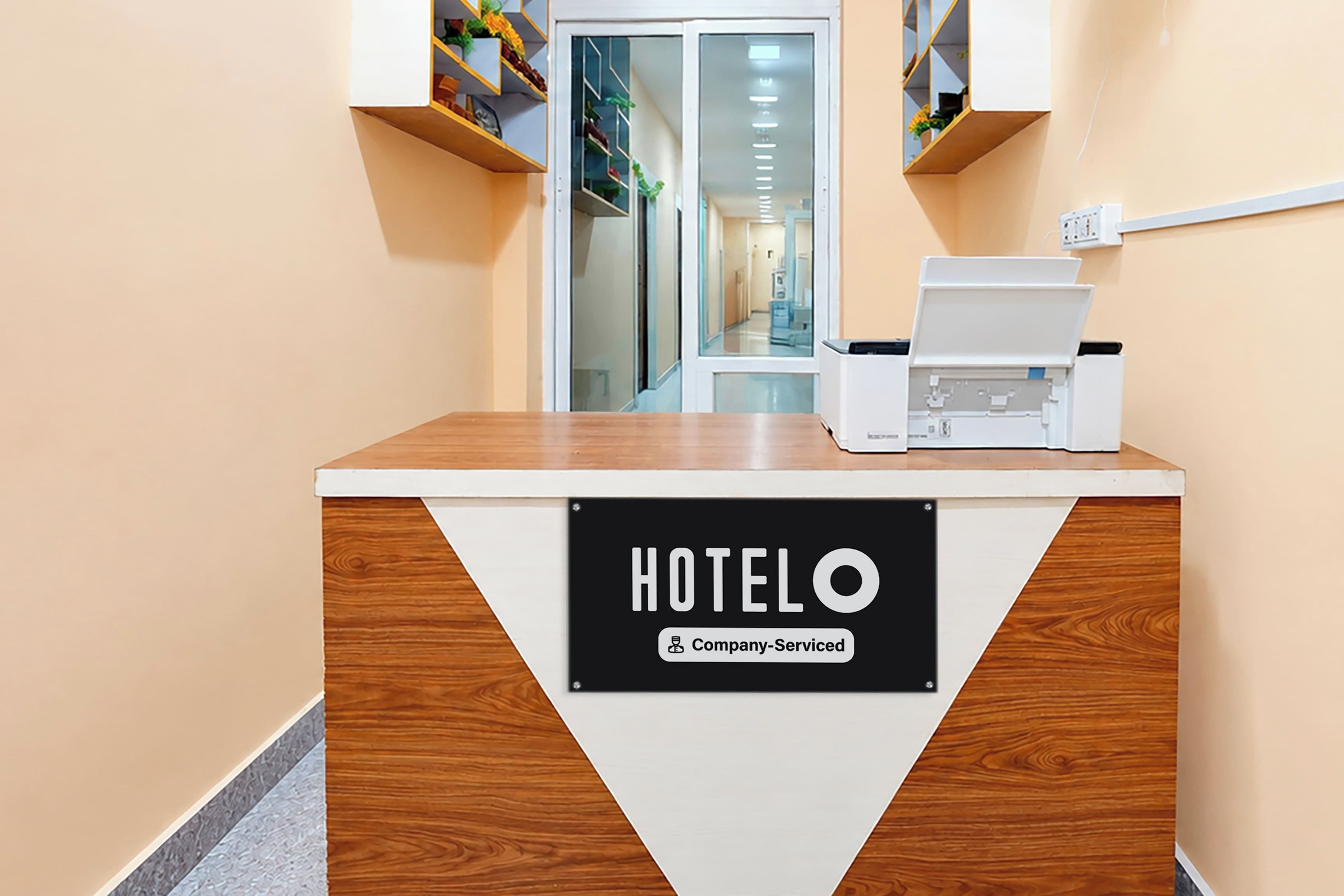 Un comptoir d’accueil avec une pancarte indiquant « HOTELO Company Serviced » et une imprimante posée dessus.
