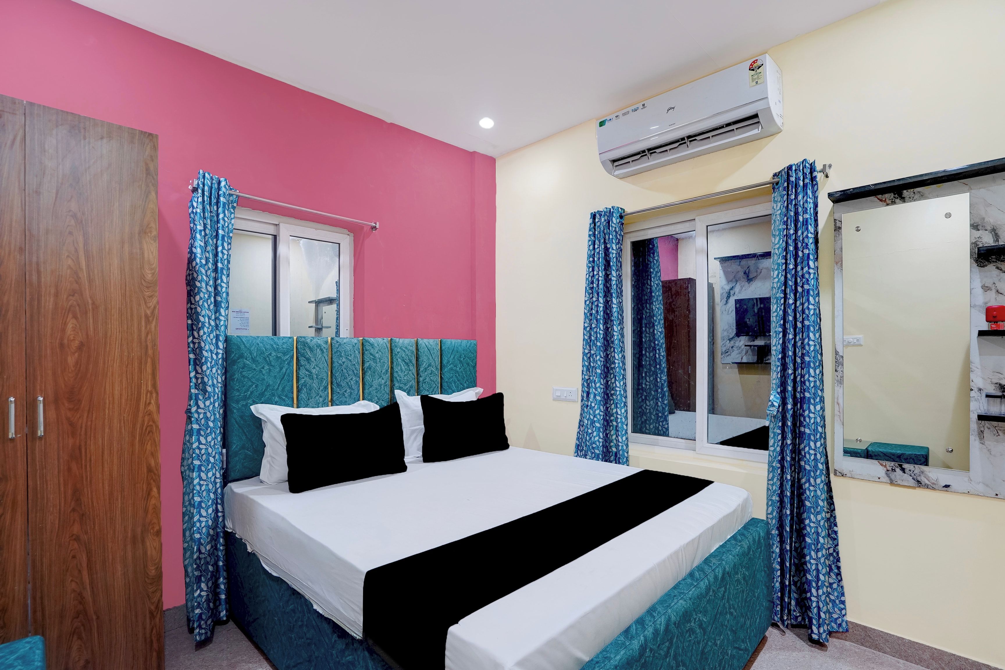 Habitación de hotel con cama, armario, ventana con cortinas, aire acondicionado y espejo.