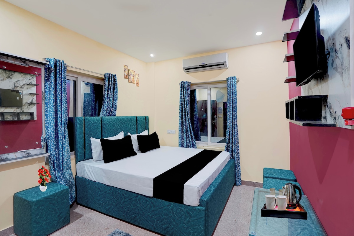 A hotel room with a bed, a TV, an air conditioner, and a window with curtains.