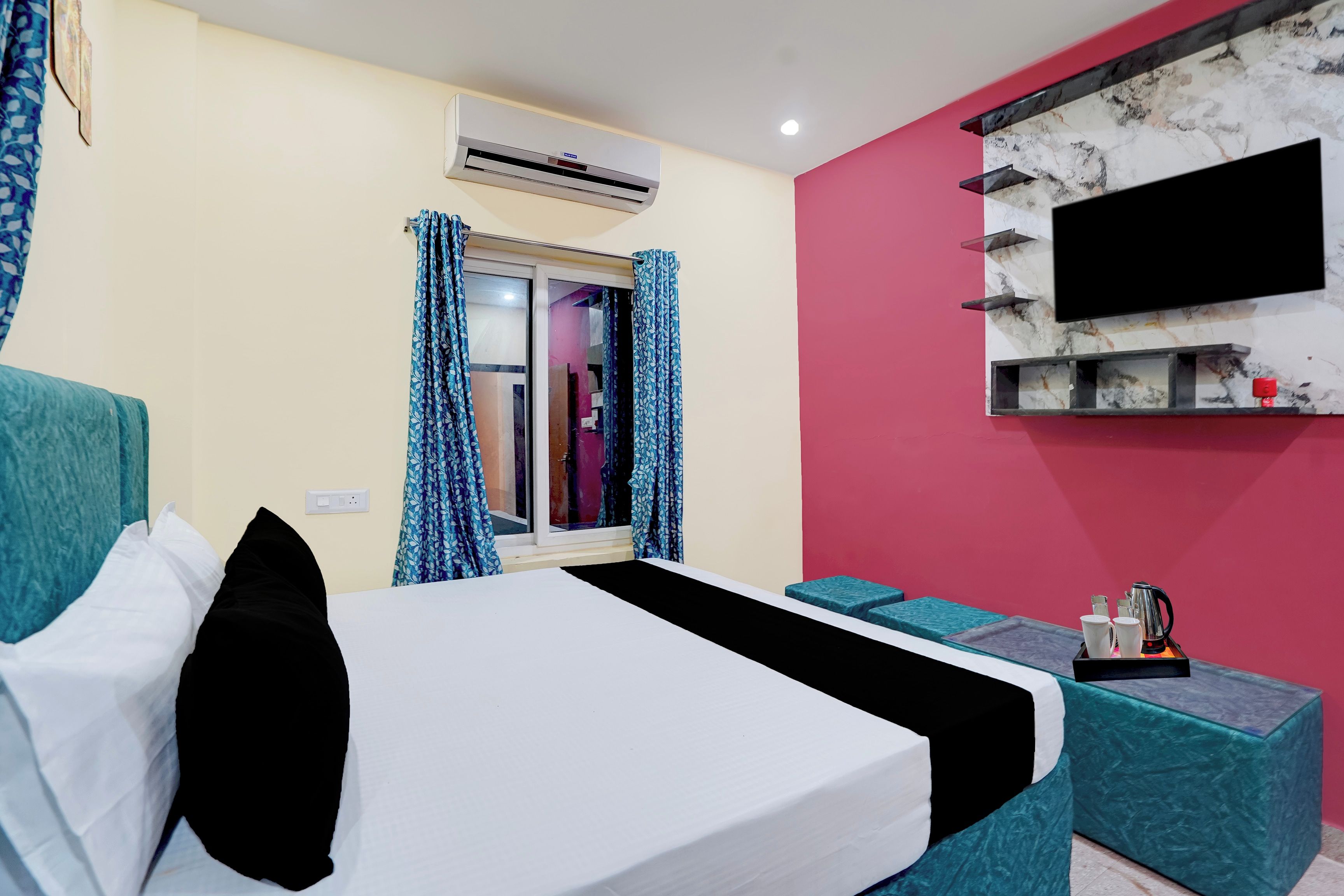 A hotel room with a bed, a TV mounted on the wall, and a window with curtains.