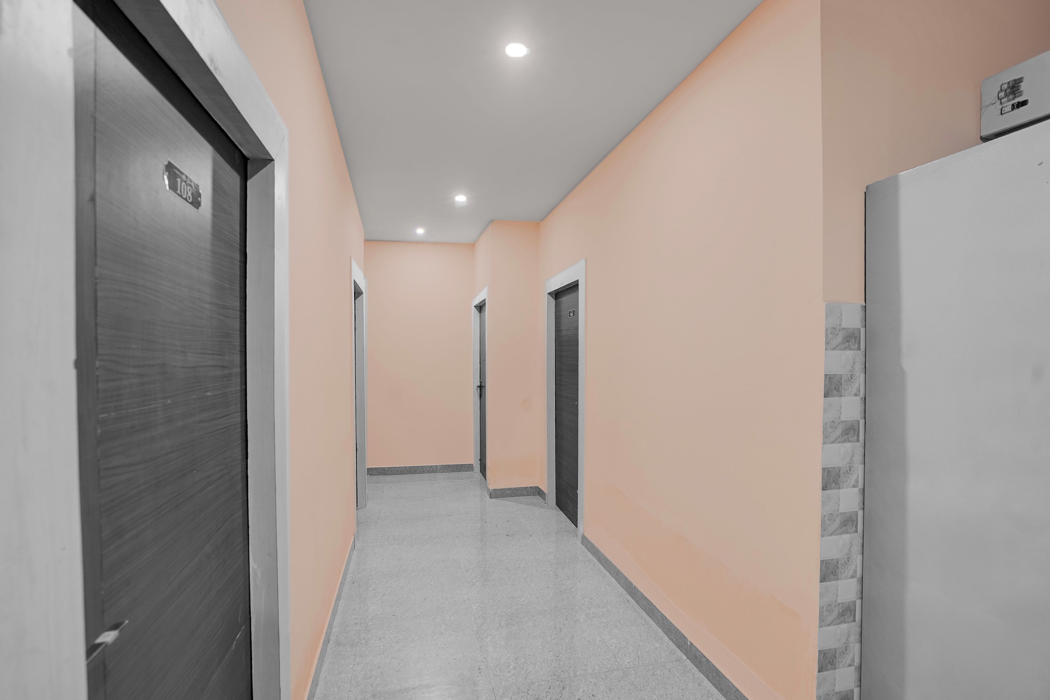 Un pasillo con puertas a ambos lados, suelo de baldosas e iluminación empotrada en el techo.