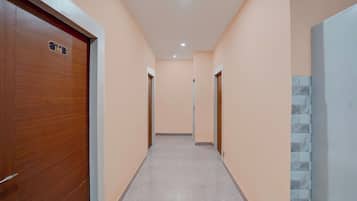 A corridor with a wooden door on the left, a tiled wall on the right, and a tiled floor.