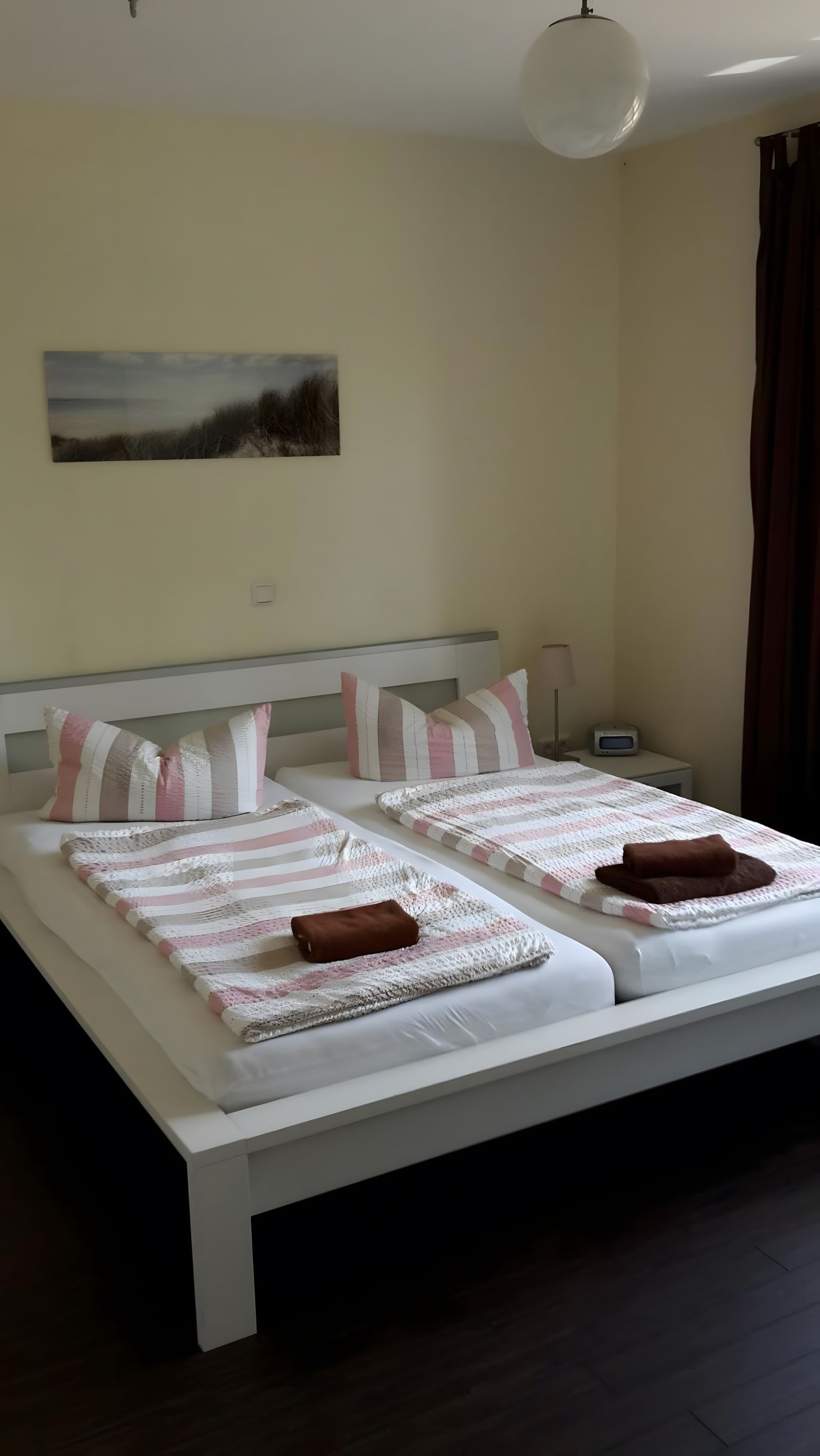 Ein Doppelbett mit gestreifter Bettwäsche und Kissen, ein Nachttisch mit einer Lampe sowie ein Wandbild.
