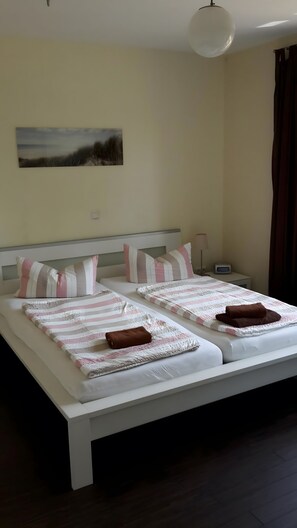 A double bed with striped bedding and pillows, a bedside table with a lamp, and a wall-mounted painting.