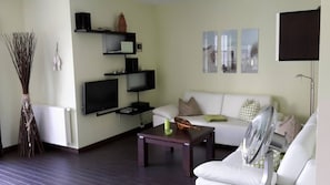 A living room with a white sofa, a coffee table, a TV, and a fan.