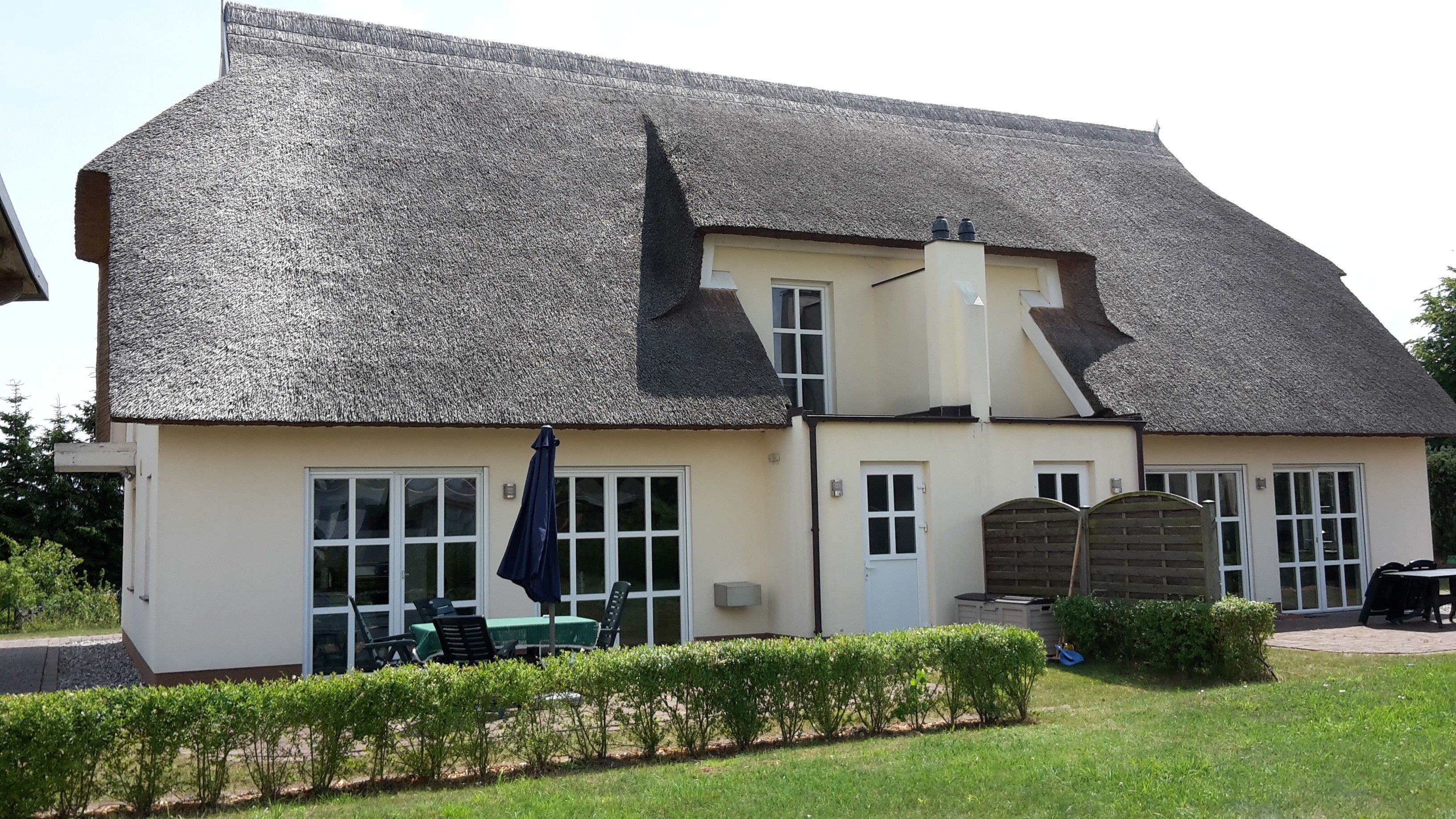 A two-story building with a steeply pitched roof, a front entrance with a door, and a small porch area with outdoor seating.