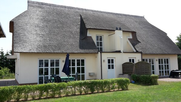 A two-story building with a steeply pitched roof, a front entrance with a door, and a small porch area with outdoor seating.