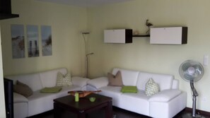 Un salon avec un canapé blanc, une table basse et un ventilateur sur pied.